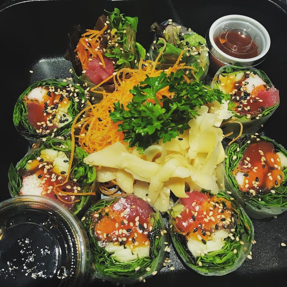 Fresh Thai Delight Broadway spring rolls with tuna, vegetables, sesame seeds, and sauces in a black dish.