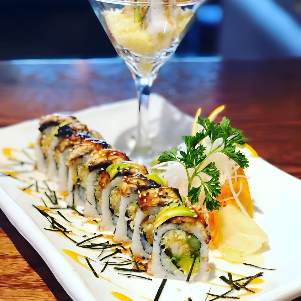 Dragon roll sushi with avocado and eel, garnished with ginger, parsley, and a martini glass.