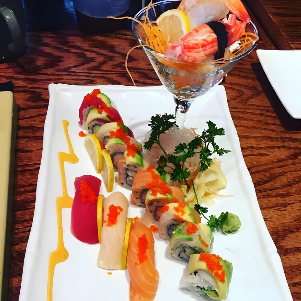 A vibrant sushi and sashimi platter with various rolls, nigiri, and a martini glass of seafood.