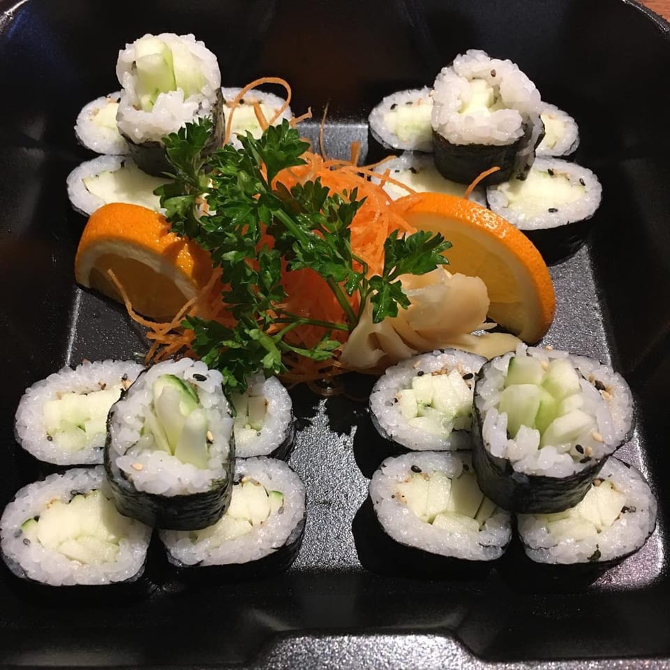 Cucumber sushi rolls with parsley, shredded carrots, and orange slices on a black plate.